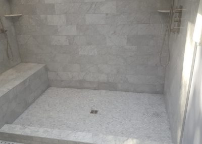 A shower with marble tile and a bench.