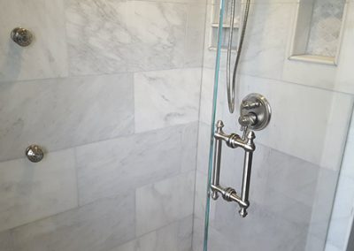 A bathroom with marble walls and floor, and glass shower door.