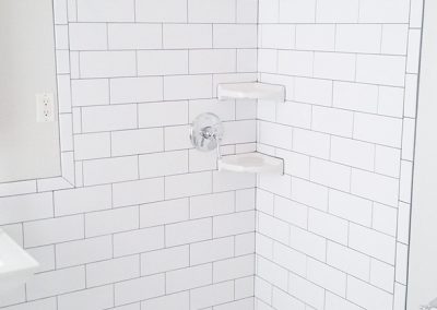 A white tiled shower with a corner shelf.